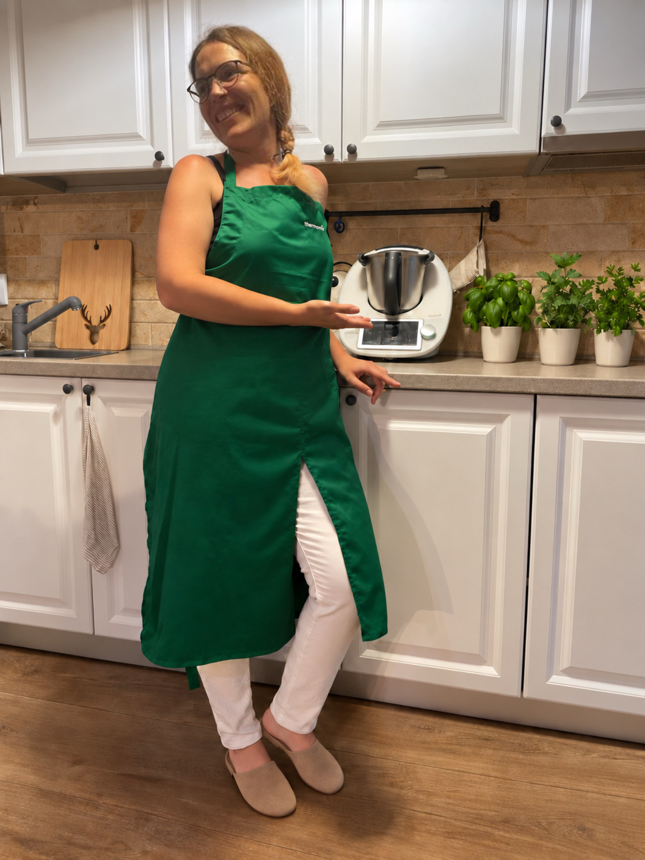 Carmen în bucătăria ei, cu șorț verde, lângă Thermomix și ghivece cu plante aromatice